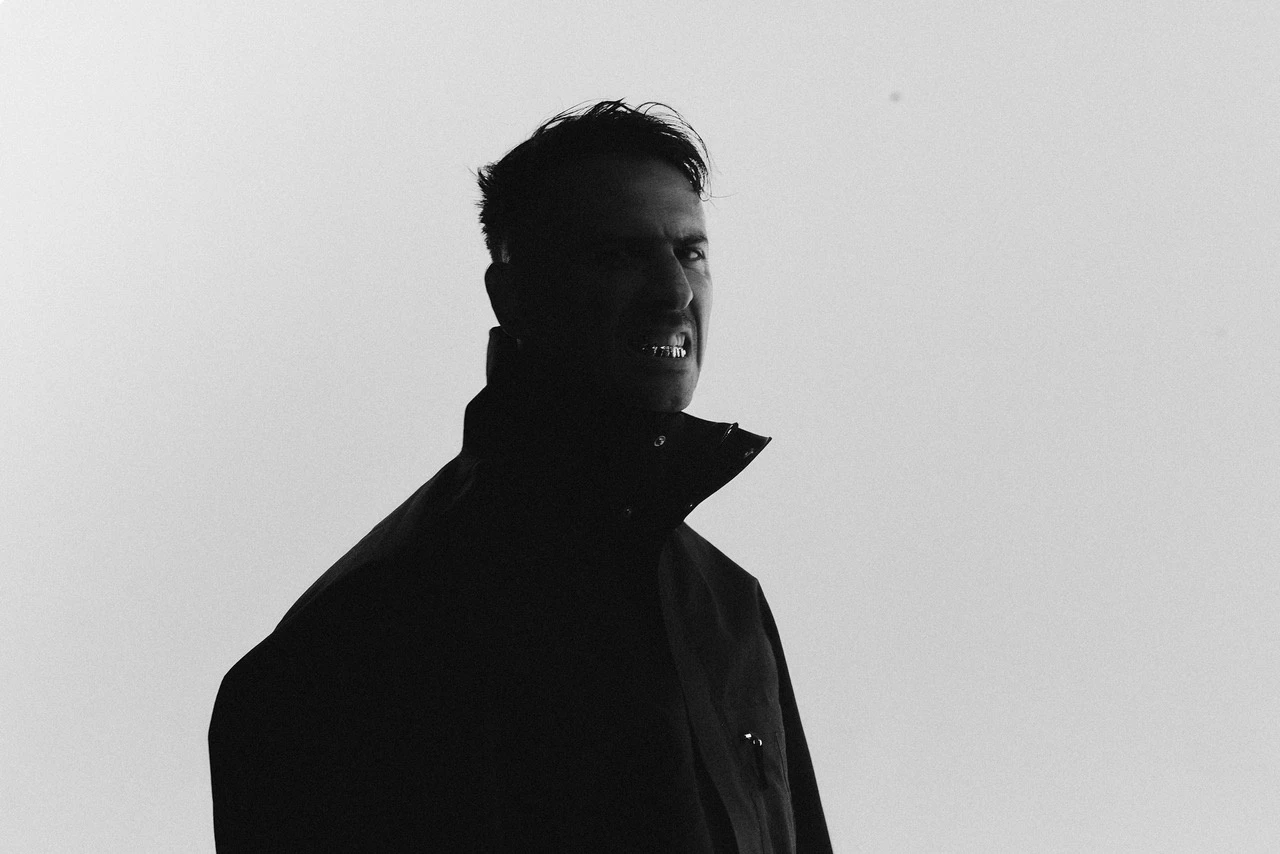 Boys Noize em foto preto e branco, de casaco escuro com gola alta, em silhueta contra um fundo claro