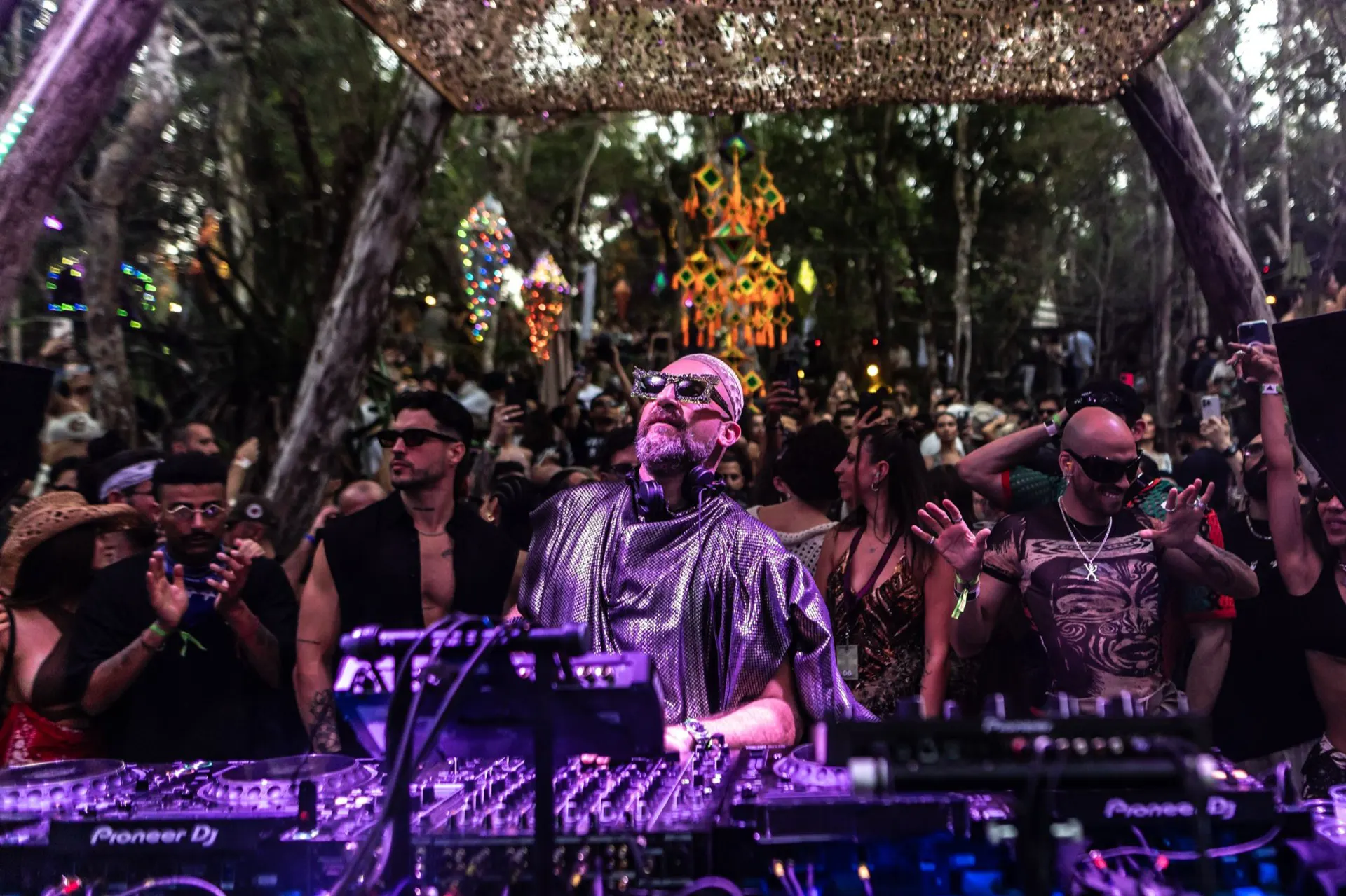 Damian Lazarus tocando atrás dos CDJs no palco do Day Zero, cercado pelo público em meio à mata