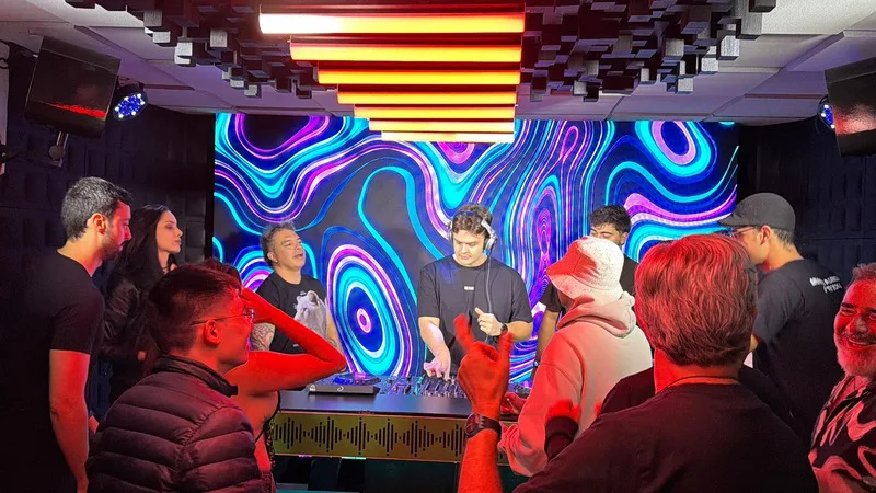 Grupo de pessoas reunidas em volta do DJ, sorrindo e conversando durante o set no estúdio 1 da DJ Ban EMC