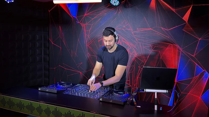 DJ tocando na cabine do Estúdio 1 da DJ Ban EMC, com painel de LED ao fundo