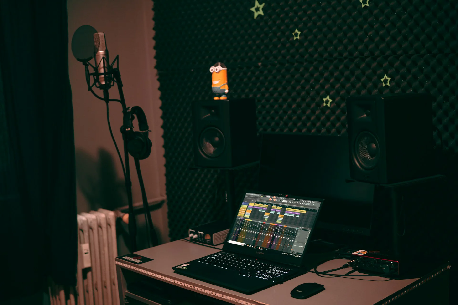 Laptop aberto numa DAW, monitores de estúdio e microfone ao fundo, num home studio